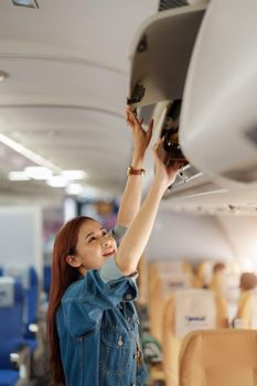 Portrait of an Asian woman putting her luggage in the luggage compartment while waiting for an economy class flight. Travel concept, vacations, tourism.