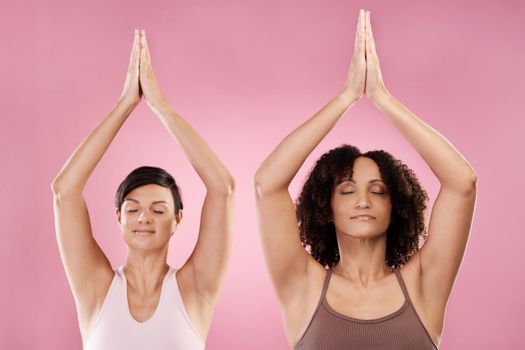 two attractive young female athletes meditating in studio against a pink background.