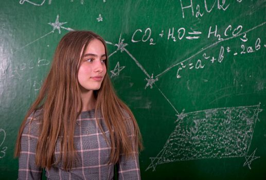 Student girl standing near clean blackboard in the classroom.