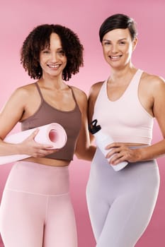 Cropped portrait of two attractive young female athletes posing in studio against a pink background.