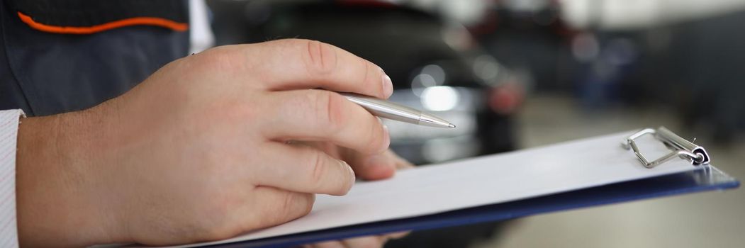 Close-up of male service worker fill maintenance documentation after fixing car. Professional mechanic work in garage. Car service, pit stop, handy concept