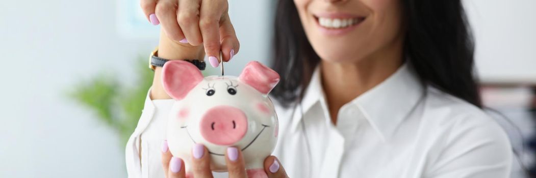 Portrait of happy woman putting coins in piggybank container and smiling. Save money, collect cash, take care of tomorrow. Saving up, investment, concept