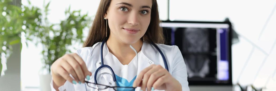 Portrait of young woman doctor sit in office at work in hospital. Intern wait for patient on appointment wear stethoscope tool. Healthcare, help concept