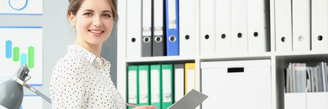 Portrait of smiling employee woman posing in conference room, making notes on paper. Businesswoman report on business meeting in company. Biz firm concept