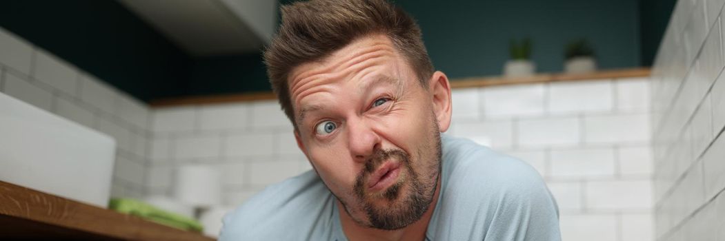 Portrait of man with funny facial expression on toilet seat, fulfill natural need. Man in bathroom with modern interior. Wc, hygiene, nature calls concept