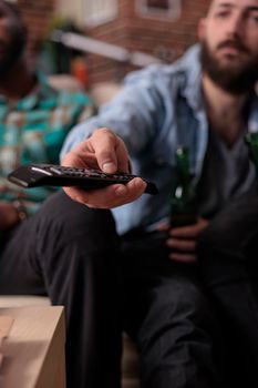 Young person using tv remote control to switch channels or television programs to find movie to watch with group of people at gathering. Searching film or tv show for fun leisure activity. Close up.