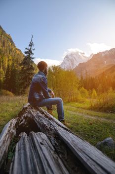 A bearded man sits on a log alone in the mountains. Healthy lifestyle concept, sunny mountain landscape.