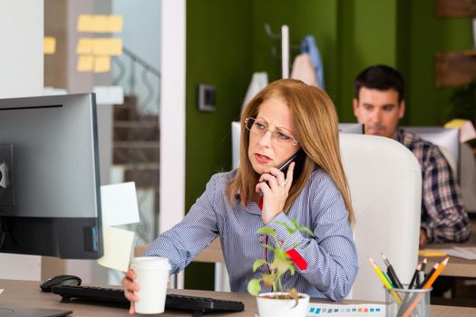 Business woman talk on the phone in the office.Looking at her monitor