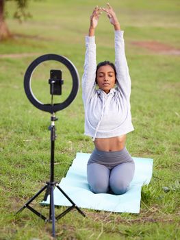 a young woman recording herself doing yoga in the park.