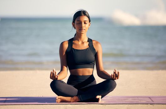 Full length shot of an attractive young woman meditating on the beach.