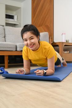 Sporty young woman doing plank on mat in living room. Fitness, sport and healthy lifestyle concept.