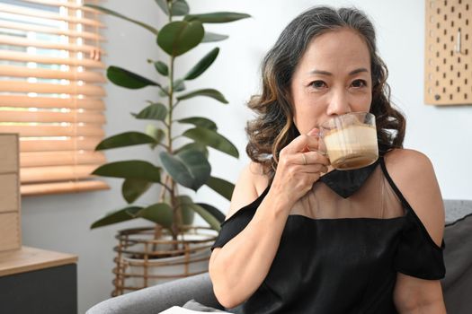 Serene middle aged woman drinking hot coffee, relaxing on couch at home. Stress free, positive mood concept.