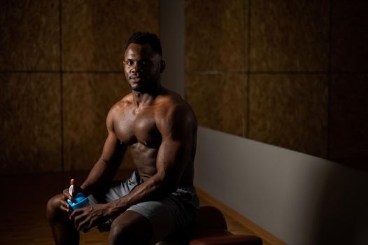 Shirtless african american man drinking from a shaker in the gym