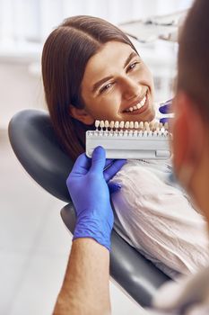 Professional doctor is choosing a colour of teeth in modern dental clinic