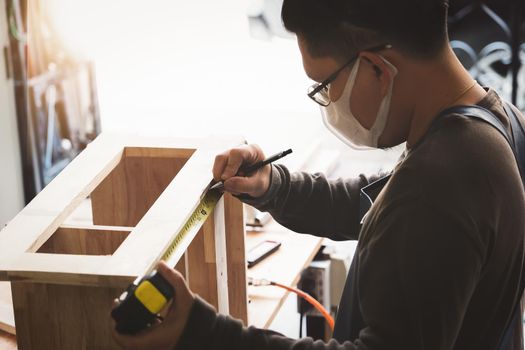 A carpenter measures the planks to assemble the parts, and build a wooden table for the customer