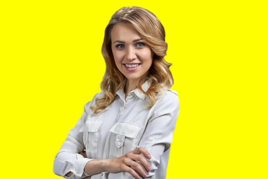 Beautiful young woman in white blouse looking at camera with crossed arms. Pretty girl posing at camera on yellow background.