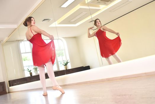 a young ballerina in a red dress and pointe shoes performs exercises in a dance studio