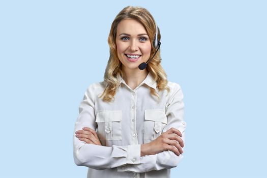 Happy call center operator with headset crossing arms on blue background. Support agent at work.
