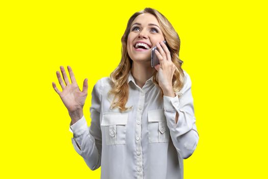 Joyful young woman in formal blouse talking on mobile phone on yellow background. Happy smiling woman talks on cell phone against color background.