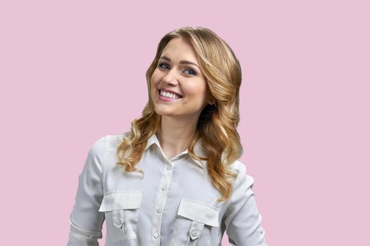 Beautiful smiling young woman in white blouse posing at camera. Charming lady on pink background.