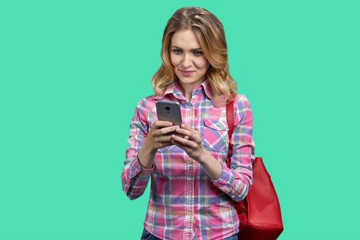 Young smiling woman using smartphone while standing color background. People, modern technology and lifestyle concept.