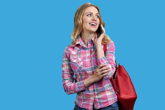 Pretty smiling girl having phone conversation standing on blue background. Happy young woman talking on mobile phone on color background.