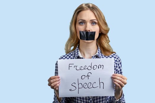 Young woman with taped mouth on blue color background. Young beautiful woman with black tape on her mouth. Freedom of speech concept.