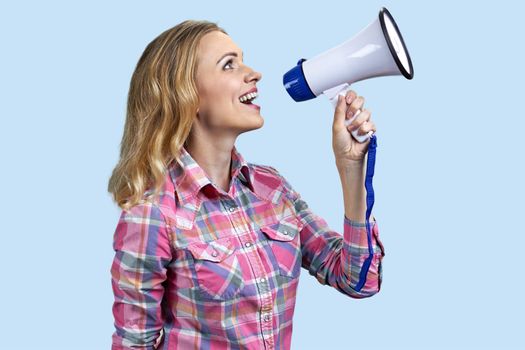 Side view of young pretty woman talking into megaphone. Woman talks in loudspeaker on color background.