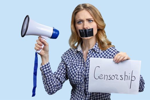 Woman with taped mouth holding megaphone on light blue background. Taped mouth woman can not speak.