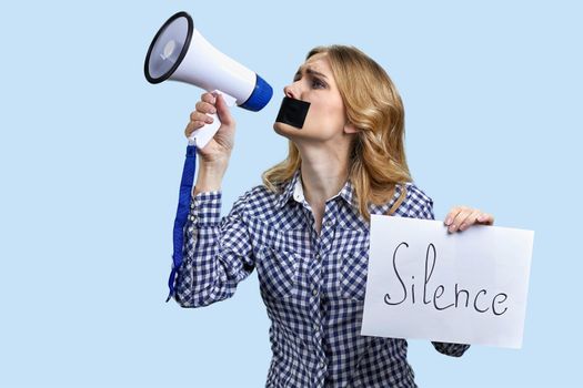 Upset woman protester with adhesive tape over mouth trying to speak in megaphone. Free speech.