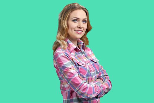 Pretty smiling woman wearing checkered shirt looking at camera with crossed arms. Beautiful girl posing at camera on color background.