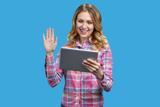 Young cheerful woman having a video call on color background. Young smiling woman holding digital tablet and waving with hand.