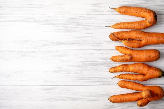 Top view close-up of several ripe orange ugly carrots lie on a light wooden surface with copy space for text. Selective focus.