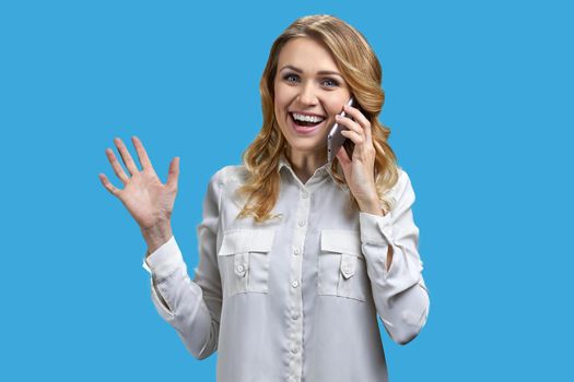 Overjoyed young woman talking on cell phone against blue background. Happy news concept.