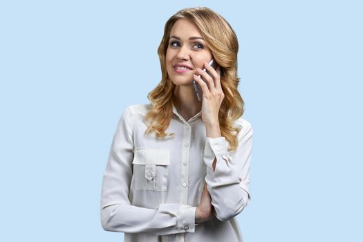 Attractive young woman talking on mobile phone and smiling. Pretty woman talks on cell phone on blue background.