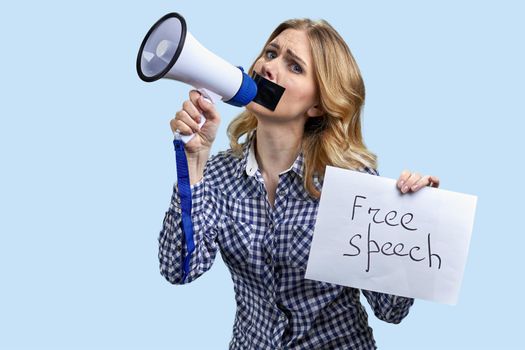Young woman with taped mouth trying to speak into megaphone. Free speech concept.