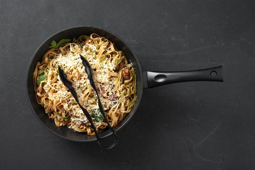 Italian pasta in a skillet with mushrooms and cream sauce on a black background. Top view. Blank space for text. Linguine pasta with mushrooms, white cheese, spinach and garlic. Healthy eating. Vegetarian food. Diet