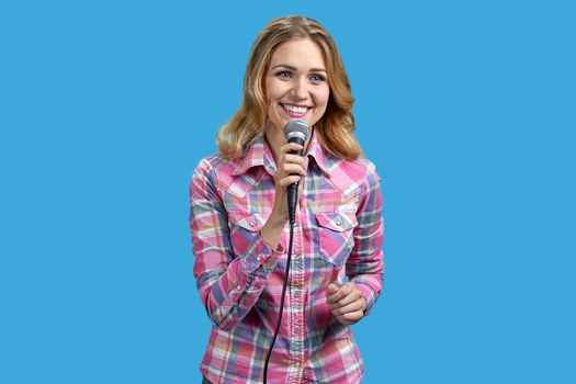 Young smiling woman holding microphone standing on color background. Woman speaker on blue background.