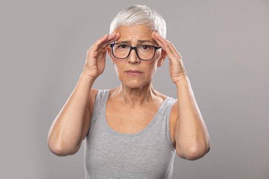 Headache migraine. Worried expression. Senior old woman with short gray hair and glasses show headache problems, healthcare and medicine concept