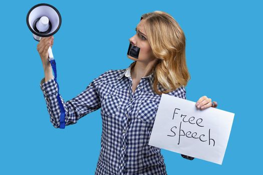 Upset woman protester with adhesive tape over mouth looking at megaphone in her hand. Free speech.