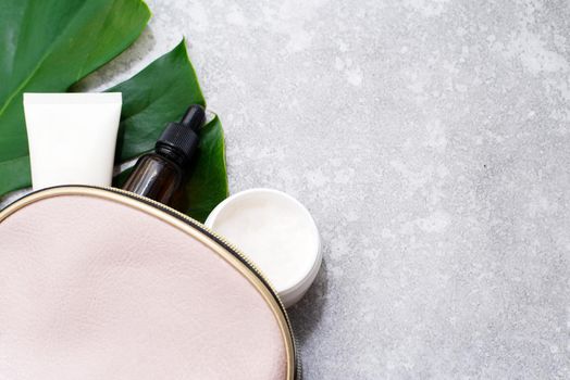 Cosmetic bag with serum and moisturizer on a tropical monstera leaf on a gray background with copy space.