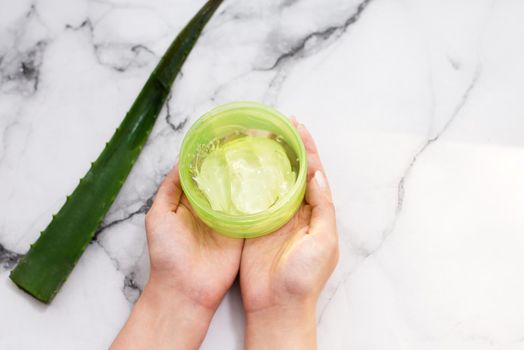 Female hands holding aloe gel on marble background.