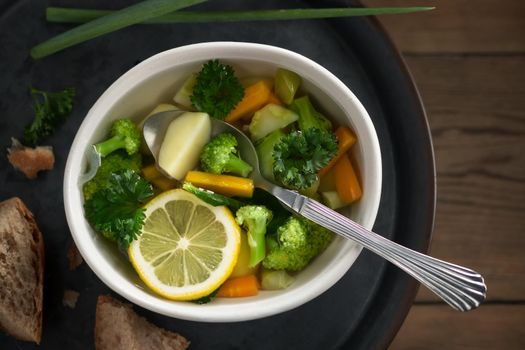 Vegetarian vegetable soup with carrots, broccoli and parsley in a light bowl on a metal tray on a wooden table.