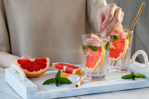 Girl cooking summer refreshing fruit cocktail with grapefruit slices and mint.