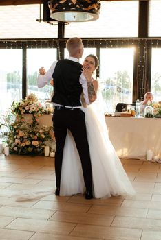 the first wedding dance of the bride and groom inside the restaurant hall in sunset light