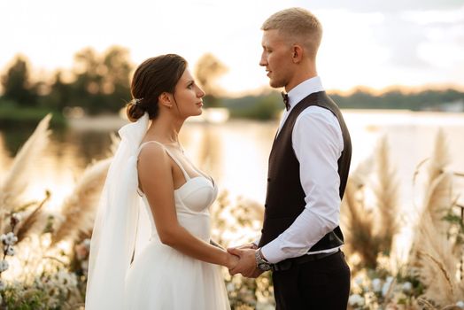 bride and groom against the backdrop of a yellow sunset on a pier near the river