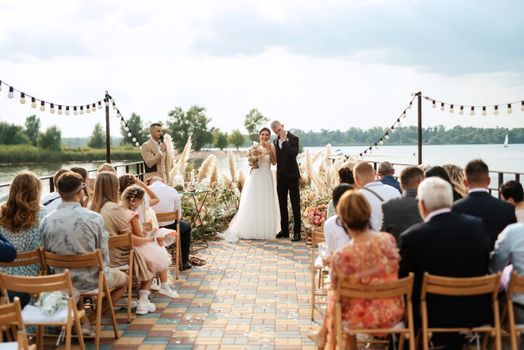 wedding ceremony on a high pier near the river with invited guests