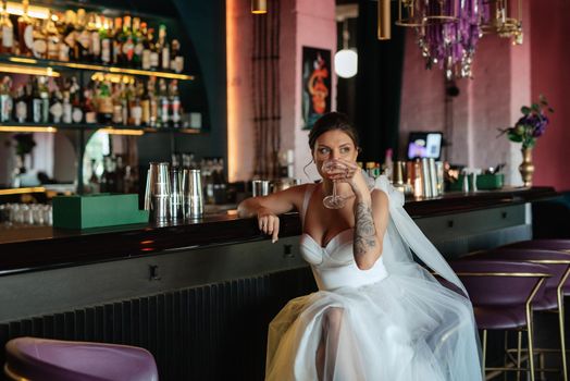 bride inside the cocktail bar at the bar in a bright atmosphere with a glass of drink