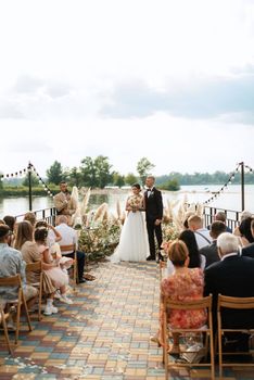 wedding ceremony on a high pier near the river with invited guests