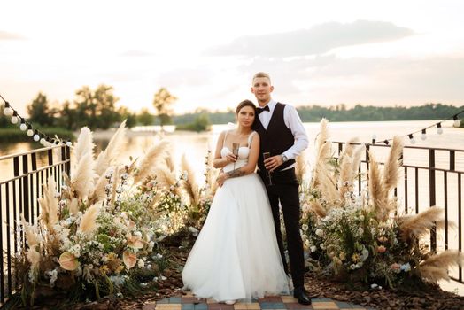 bride and groom against the backdrop of a yellow sunset on a pier near the river